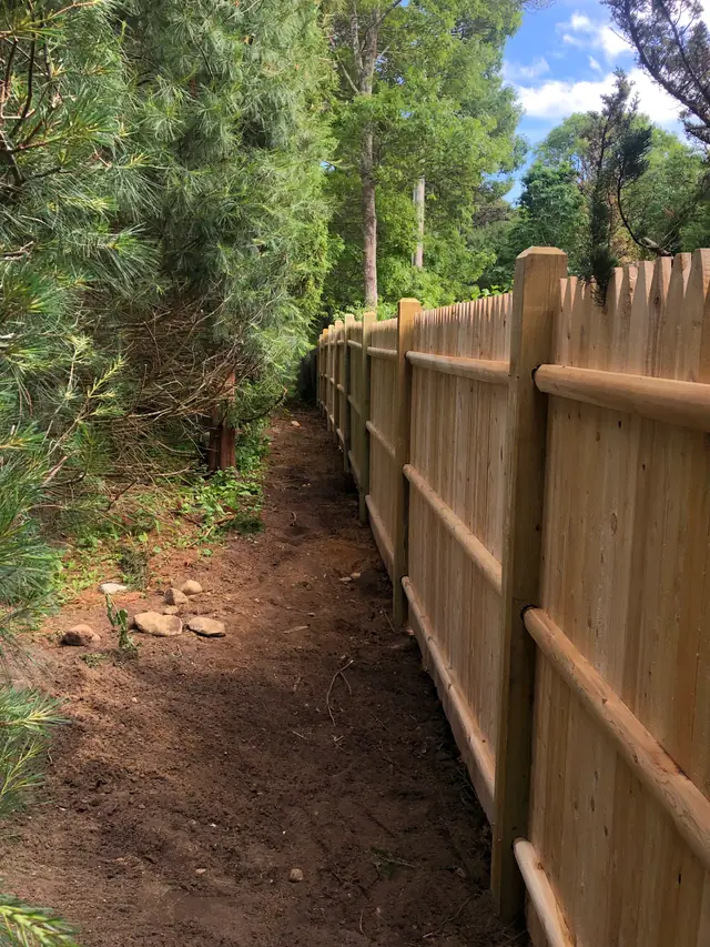 A new cedar stockade fence run by Landmark Fence along a wooded path in North Eastham
