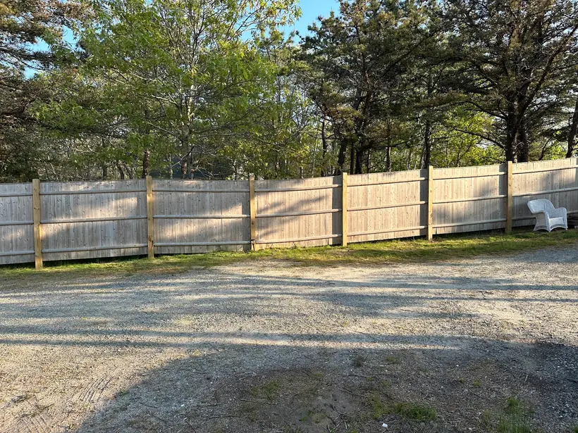 A finished Landmark Fence board privacy run along a gravel drive under Cape Cod pitch pines